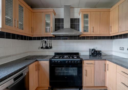 GoodmayesUksas 4 bed house Free parking的厨房配有木制橱柜和黑炉灶烤箱。