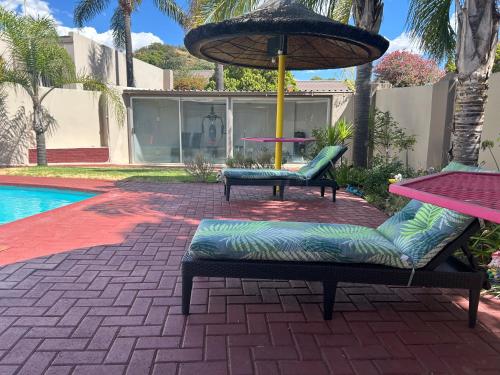 布隆方丹SiBella guest house的游泳池旁的两把椅子和一把遮阳伞