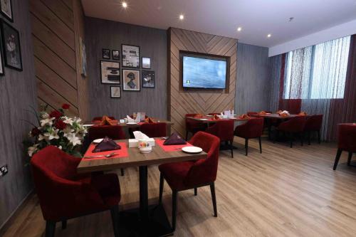 富查伊拉Fortis Hotel Fujairah的餐厅设有桌子、红色椅子和电视