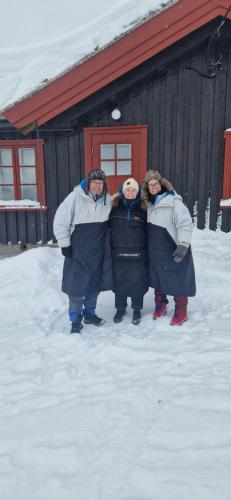 MorkSkotten Seter - Bed & Husky的三人站在一座建筑前面的雪地里