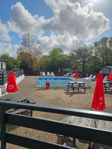 Bettws-EvanPB6的一组野餐桌,在游泳池旁边配有红色遮阳伞