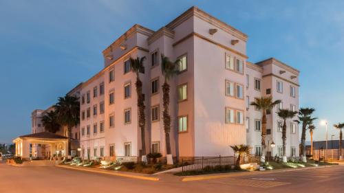 萨尔蒂约voco Saltillo Suites, an IHG Hotel的一座白色的大建筑,前面有棕榈树