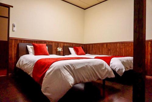 大岛露伴ロハンrohan的一间卧室配有两张红色和白色床单