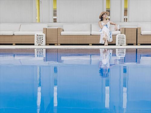 那霸Okinawa EXES Naha的坐在游泳池旁沙发上的女人