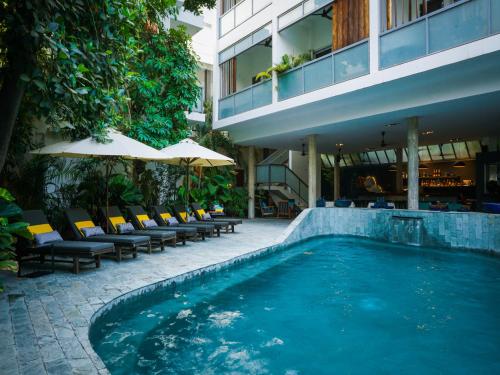 金边红毛丹酒店 - 金边的游泳池位于带椅子和遮阳伞的大楼旁