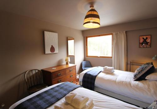 阿维莫尔Cairngorm Lodge Rothiemurchus的一间卧室设有两张床、一个梳妆台和窗户。