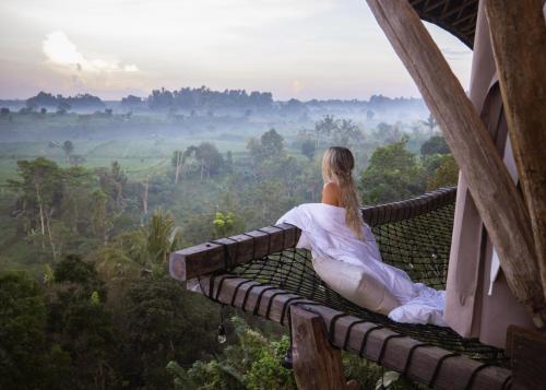 SelatCamaya Bali - Magical Bamboo Houses的坐在建筑物阳台上的身着白色服装的女人