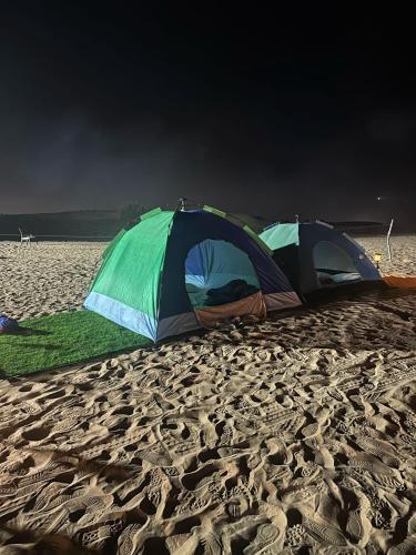 HunaywahDubai Tourism and Travel Services的沙质海滩上的两个帐篷,暴风雨临