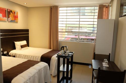 塔克纳Hotel Puma'r Tacna的酒店客房设有两张床、一张桌子和一个窗户。