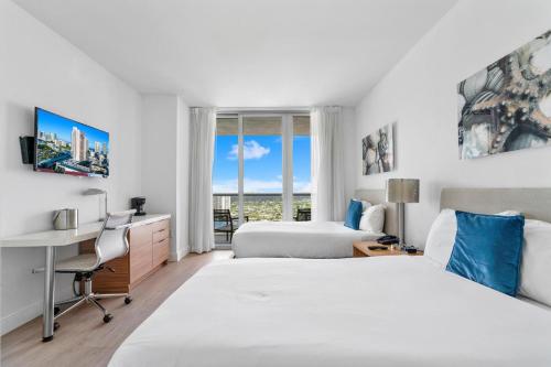 好莱坞Panoramic views Studio on the 27th floor Beachwalk的酒店客房设有两张床、一张书桌和一个窗户。