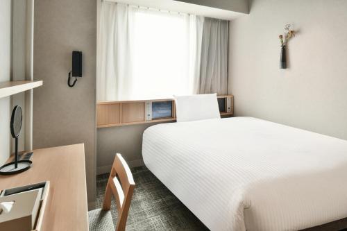 松山REF Matsuyama City Station by VESSEL HOTELS的一间酒店客房,配有一张白色的床和一张书桌