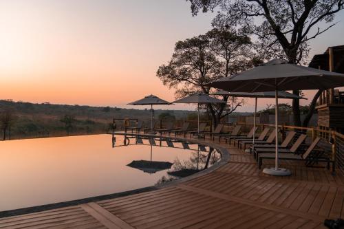 雾观Mdluli Safari Lodge的湖上带长椅和遮阳伞的木桥