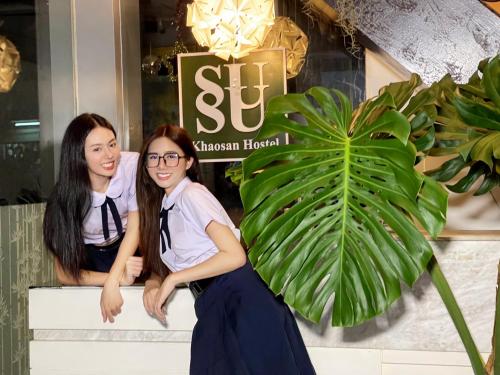 曼谷SUSU khaosan hostel的两个女孩坐在商店前面的长凳上