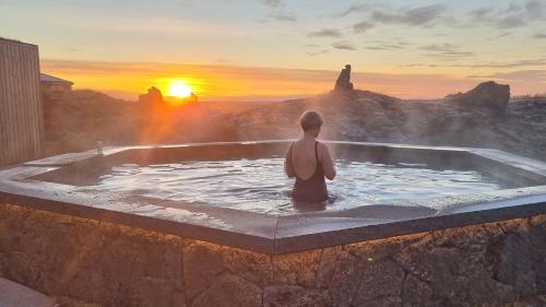 MidhraunMiðhraun - Lava resort的坐在热水浴缸中观看日落的人