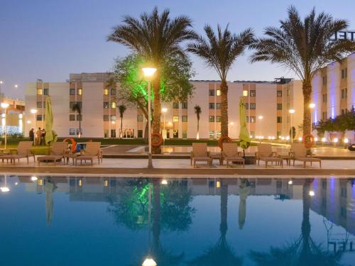 开罗诺富特开罗机场酒店的酒店前方的游泳池设有椅子和棕榈树