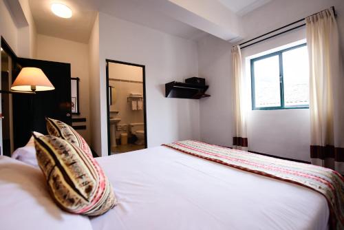 库斯科Hotel Raymi的卧室配有带枕头的白色床和窗户。