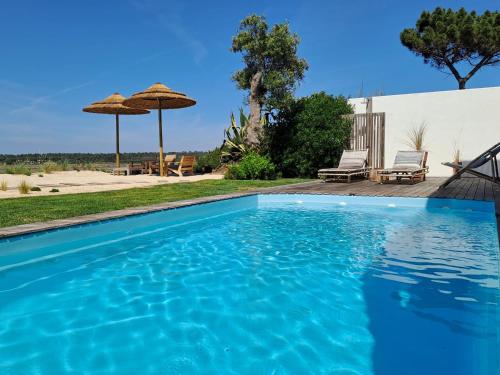 卡瓦利亚尔Casa Atlântico Carvalhal Comporta, apartamento piscina aquecida的蓝色游泳池设有两把椅子和一把遮阳伞