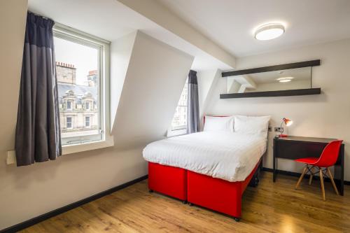 利物浦利物浦图恩酒店的一间卧室配有红色的床、一张书桌和一个窗户。