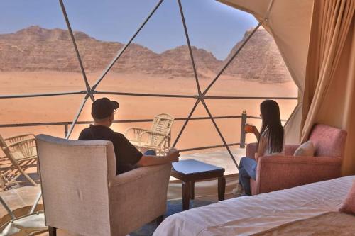 瓦迪拉姆Taj Wadi Rum camp的坐在椅子上看着沙漠的男人和女人