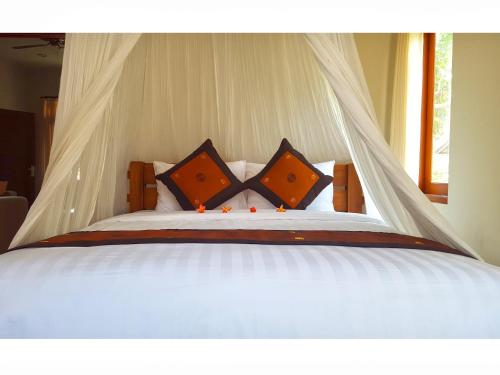 塞米亚克居安达别墅酒店的白色的床、橙色枕头和天蓬