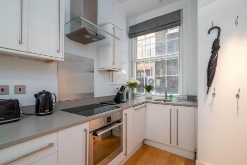 伦敦GuestReady - Stunning Covent Garden 2BR Duplex的厨房配有白色橱柜和窗户。