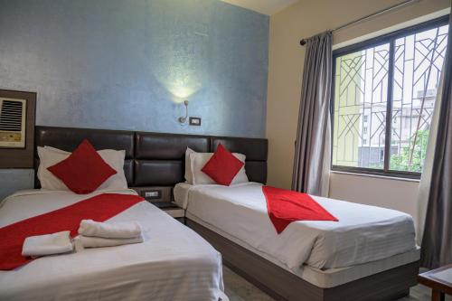 加尔各答Pallavi International的两张位于酒店客房的床铺,配有红色枕头