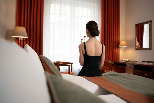 玛丽亚温泉Spa & Wellness Hotel Olympia Marienbad的站在酒店房间,望向窗外的女人