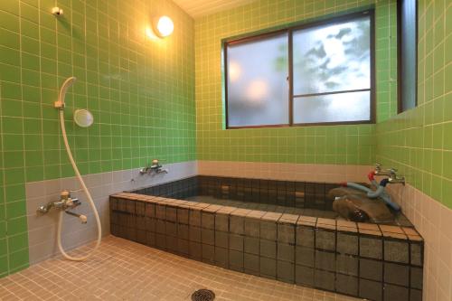 屋久岛宫之浦索日式旅馆的绿色瓷砖浴室设有窗户和浴缸