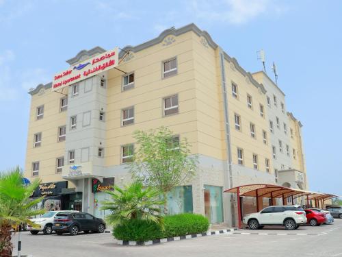 索哈尔Sama Sohar Hotel Apartments - سما صحار للشقق الفندقية的一座黄色的大建筑,停车场有车辆停放