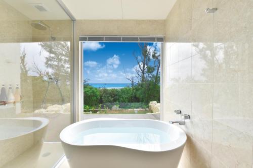 宫古岛宫古岛野费利斯别墅套房的白色的浴室设有浴缸和窗户。