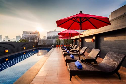 曼谷Hotel Solo, Sukhumvit 2, Bangkok - SHA Extra Plus的大楼内一个带椅子和遮阳伞的游泳池