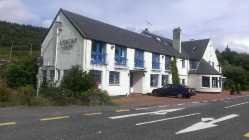 LochgairLochgair Hotel的白色的建筑,有蓝色的窗户,前面有停车位