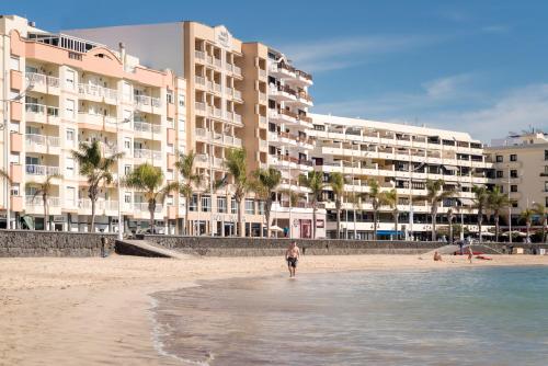 阿雷西费迪亚马酒店的站在海滩上,有建筑物的人
