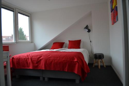 阿纳姆胡格坎普旅馆的白色卧室配有红色的床和红色枕头