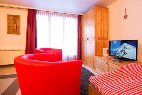 格林德尔瓦尔德MOM - Alpine Boutique Apartments, Grindelwald gletscher, Eiger View Terrace Studio的客厅配有2把红色椅子和电视