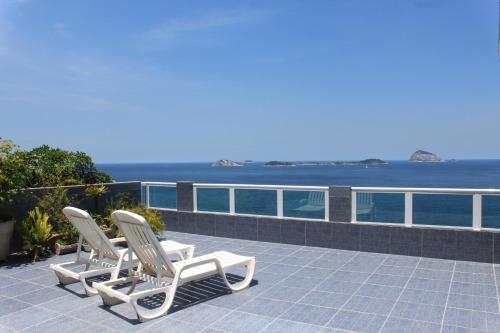 里约热内卢Hostel Vista do Mar的两把白色椅子坐在俯瞰着大海的庭院上