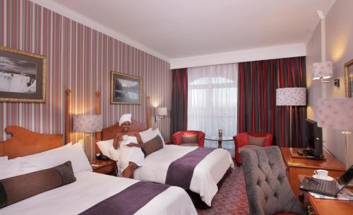 塞昆达雅园沃尔蒙特酒店的一间酒店客房,设有两张床,还有一位男士坐在床上