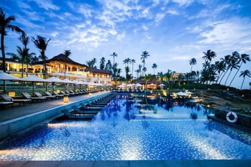 坦加拉Anantara Peace Haven Tangalle Resort的夜间带椅子和棕榈树的度假游泳池