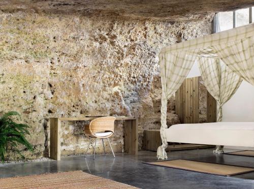 VillarrubiaCuevas del Pino Turismo Rural y Emocional SL的卧室配有一张床铺和一张椅子,位于石墙前
