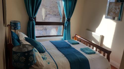爱丁堡就寝阁楼公寓11号的一间卧室配有一张带蓝色窗帘的床和一扇窗户