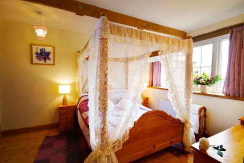 Saint CletherThe Old Wagon House的卧室配有带白色窗帘的天蓬床