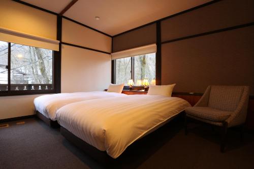 白马村Hakuba Skala Inn的一间卧室配有一张带椅子的大床和两个窗户