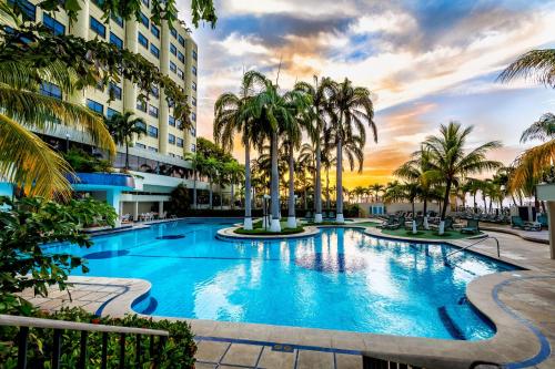 Macuto奥莱加勒比酒店的一座大型游泳池,在一座建筑前种有棕榈树