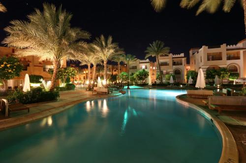 沙姆沙伊赫Rehana Royal Beach Resort - Aquapark & Spa - Family & Couples Only的棕榈树和建筑的夜间游泳池