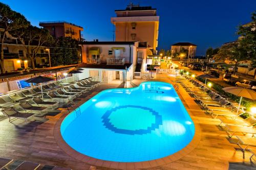 里米尼奥巴特瑞酒店的夜间游泳池,配有椅子和遮阳伞