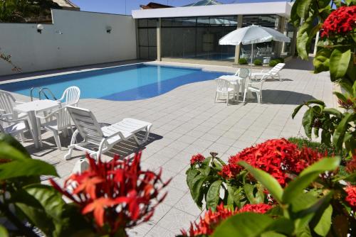 巴乌鲁Biazi Plaza Hotel的一个带白色桌椅和红色鲜花的游泳池