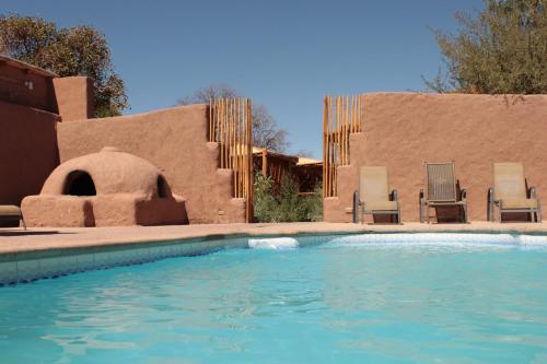 圣佩德罗·德·阿塔卡马波布拉多奇麦尔酒店的一座带两把椅子的游泳池以及一座建筑