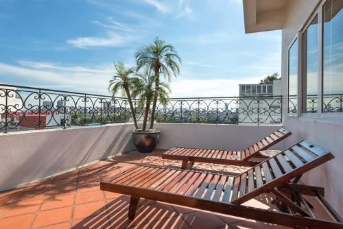 河内Hanoi E Central Luxury Hotel & Restaurant的阳台设有2个木制长椅和1棵棕榈树