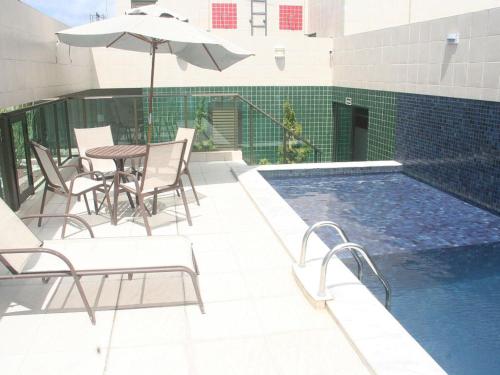 马塞约Apartamento Praia Jatiúca的一个带椅子和桌子的游泳池以及一把遮阳伞