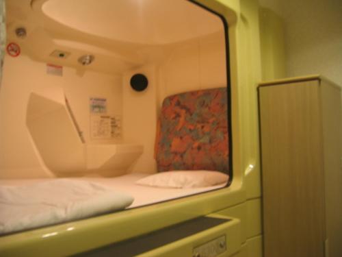 大阪斋桥格兰德桑拿胶囊旅馆的镜子里的一个床和椅子的反射